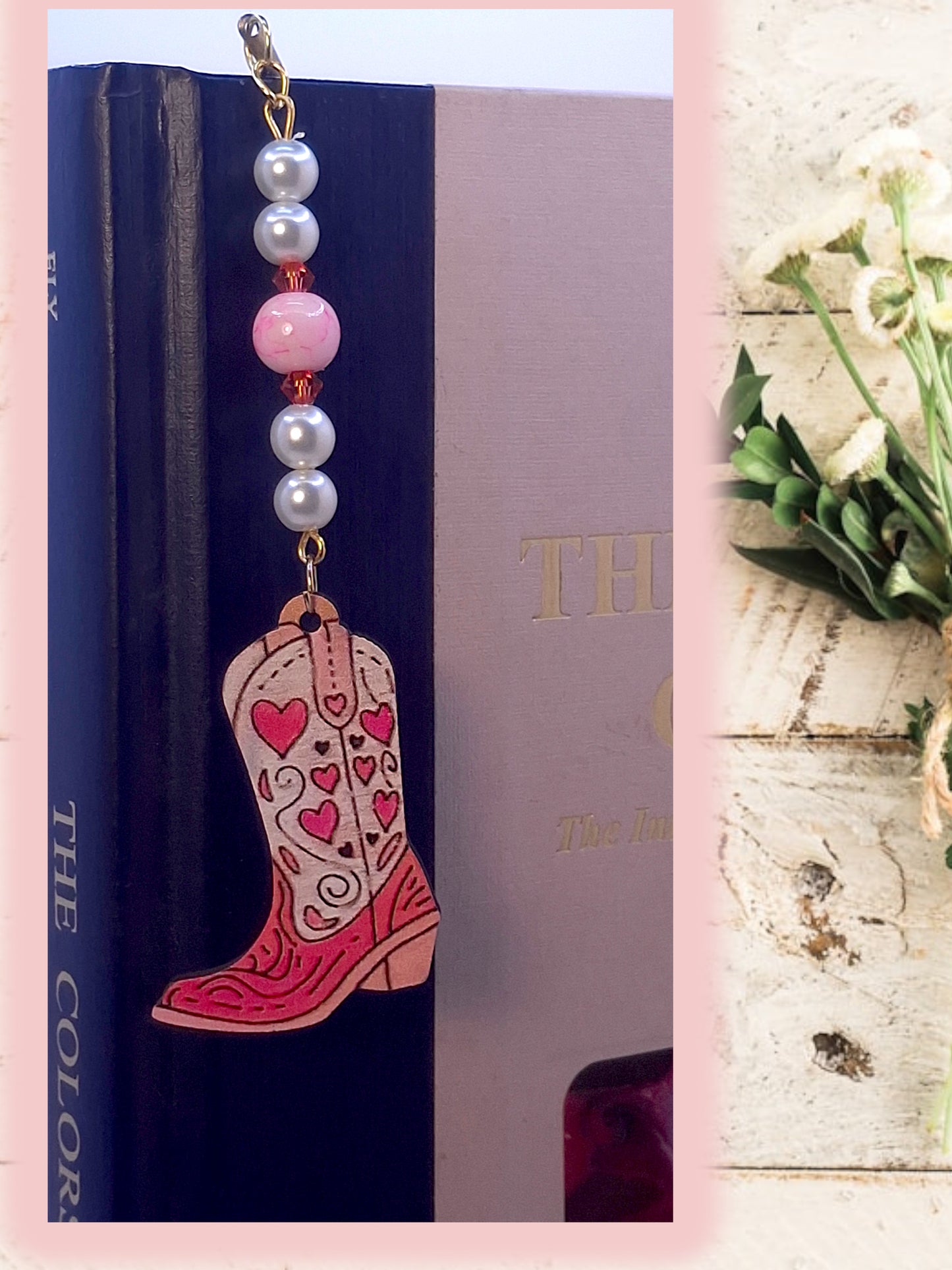 Beaded bookmark with a pink cowboy boot charm on a book, next to a vase of flowers.