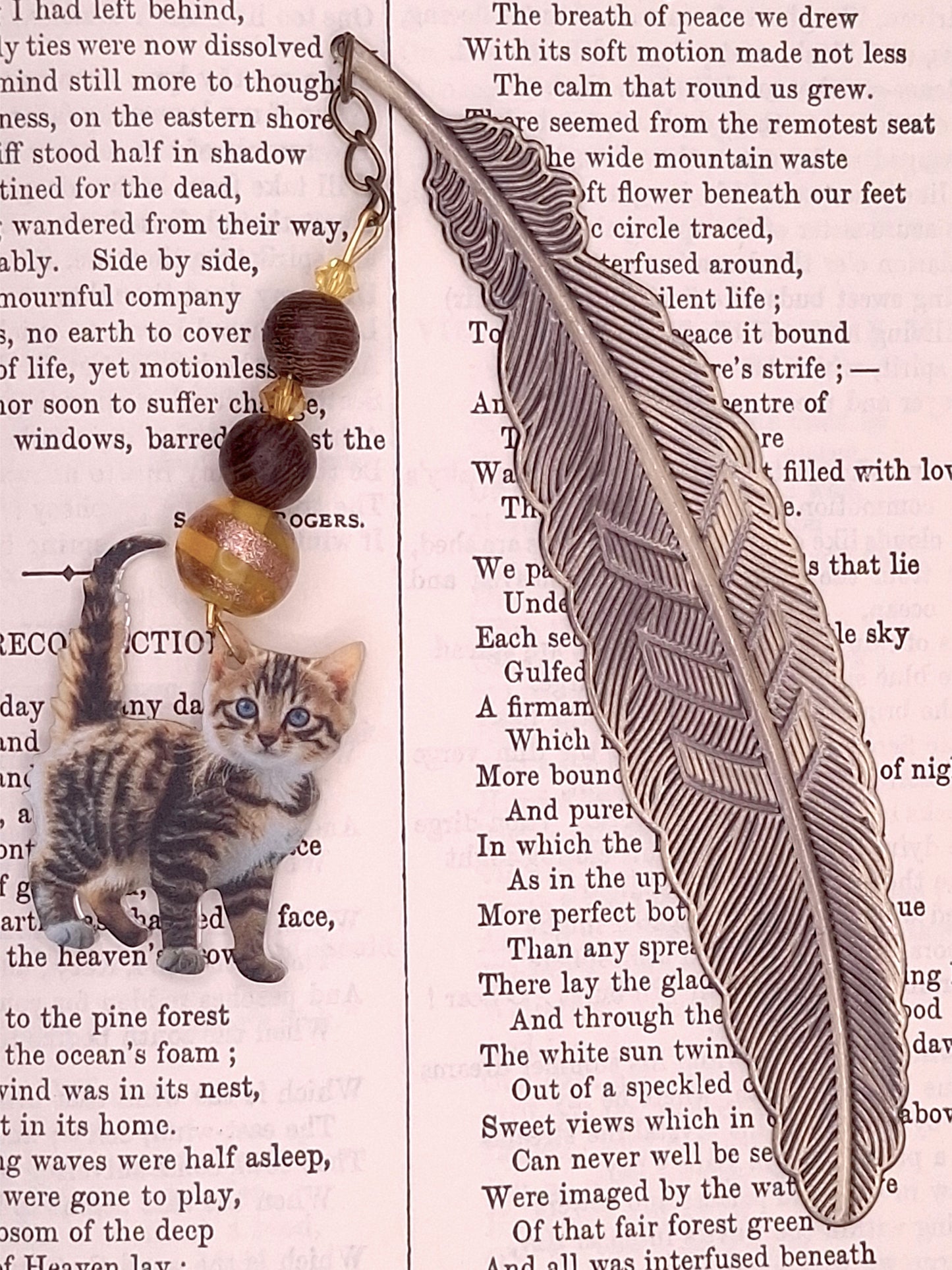 Decorative flat feather bookmark with  topaz color bead and wooden beads and tabby kitten charm a textured paper background 
