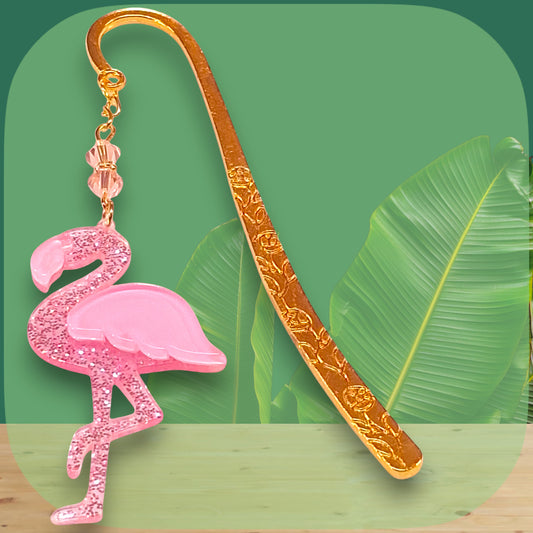 Gold bookmark etched with floral pattern with pink glitter flamingo charm on a green leaf background