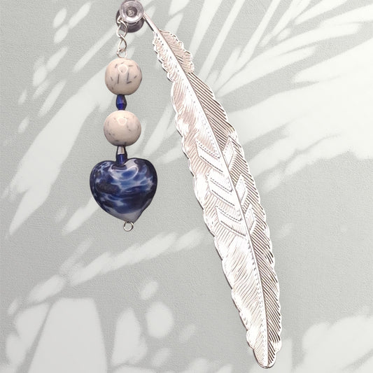 Sophisticated silver-tone flat feather bookmark with faux porcelain beads, blue glass spacers and blue willow heart charm on a light gray background