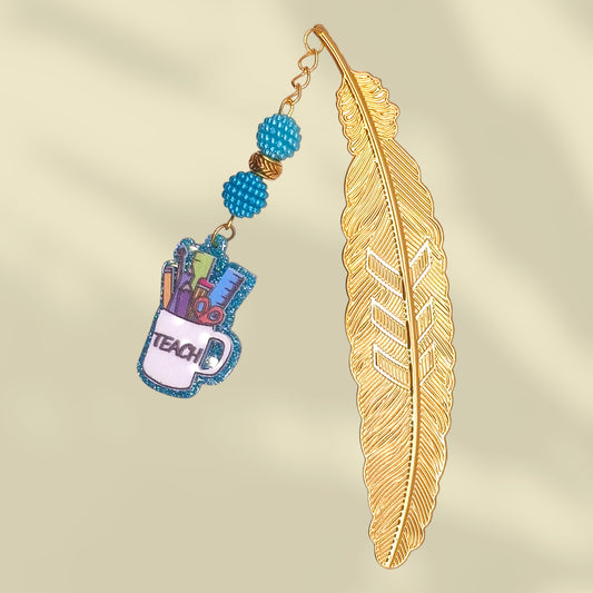 Gold feather-shaped bookmark with blue bayberry beads and cup with the word teach. Inside the cup are school tools - ruler, scissor, pen, pencil, etc.