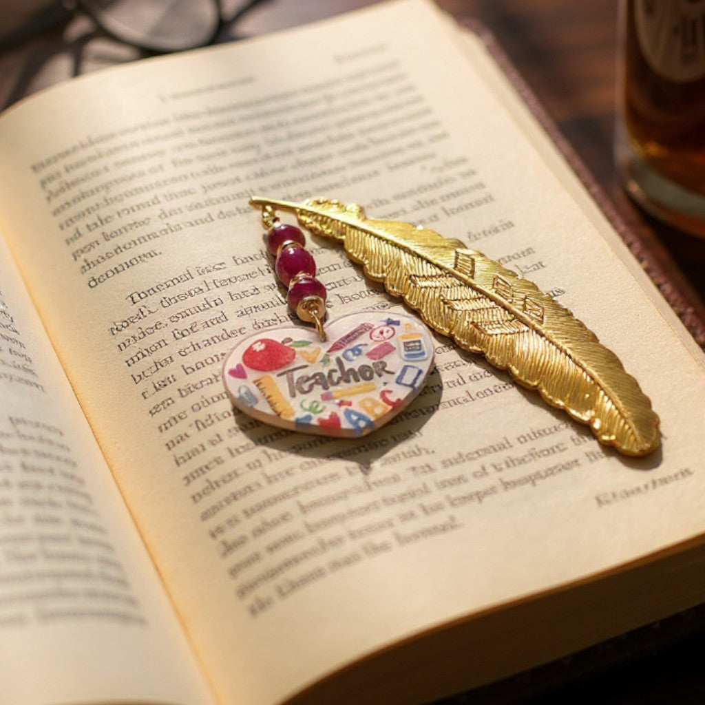 Decorative feather bookmark with a heart-shaped "teacher" charm on an open book